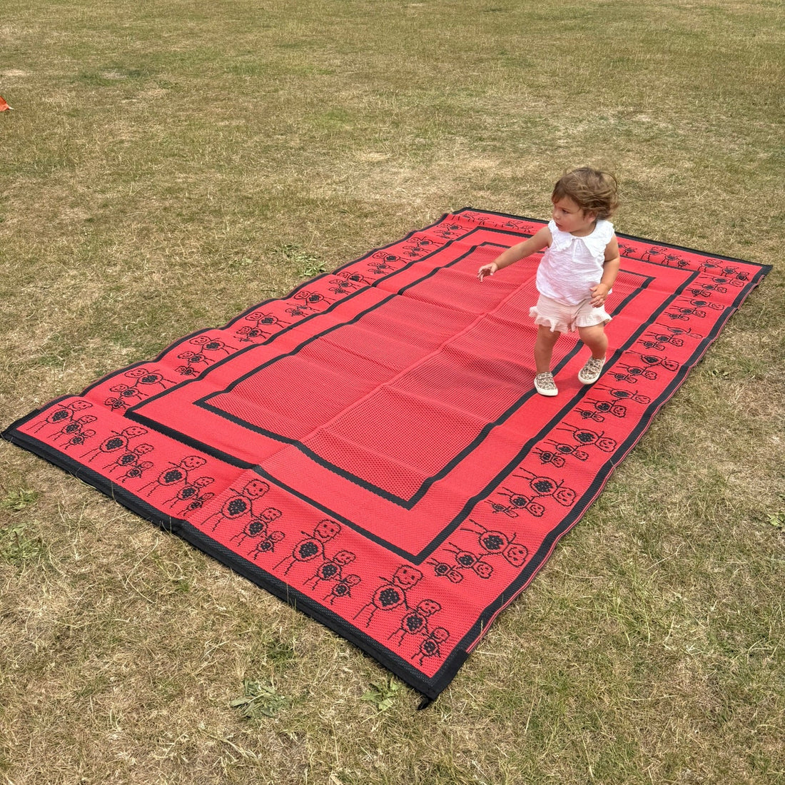 Red kids camping mat displayed outdoors on grass with decorative border illustrations