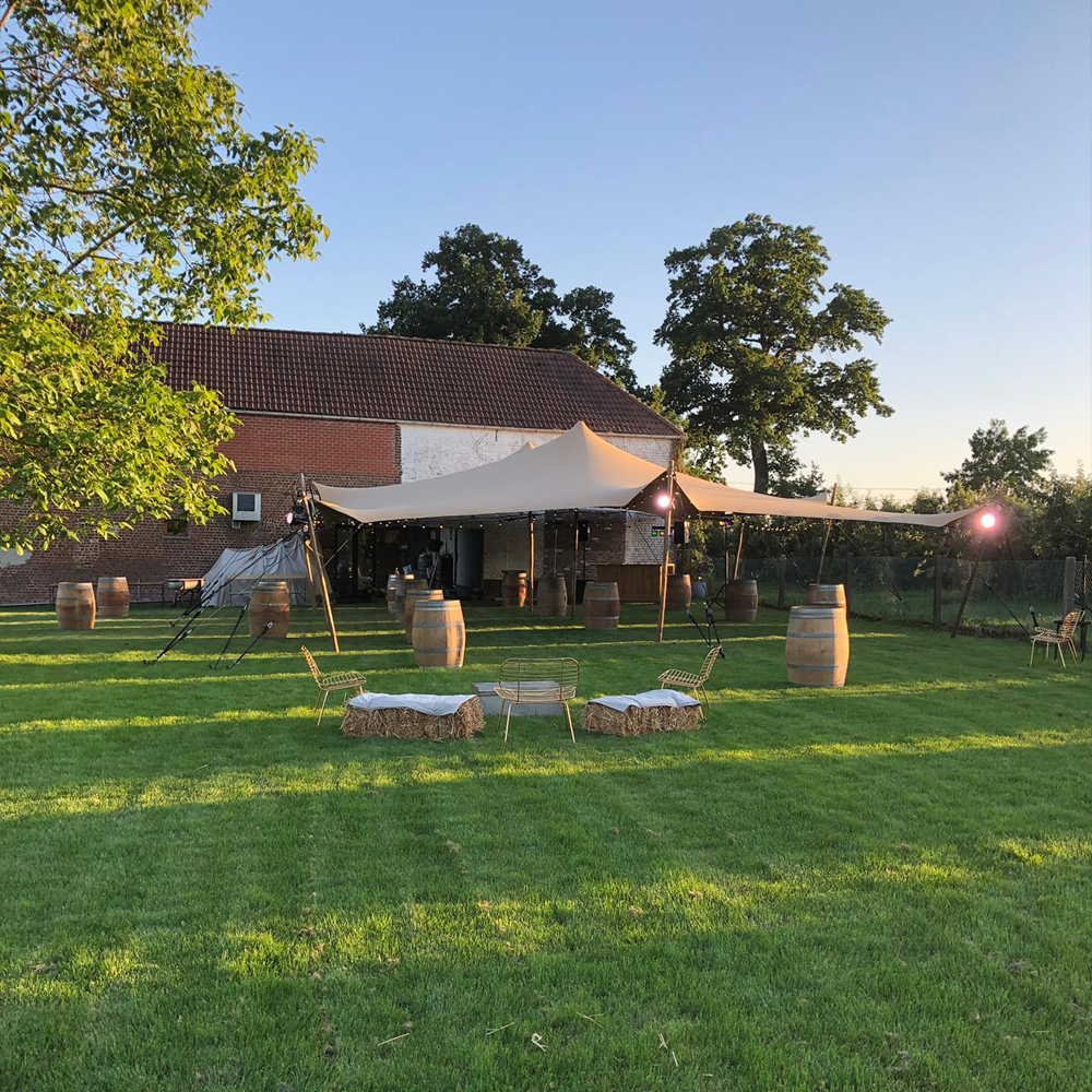 Stretch tent installed outdoors on a grassy field during sunset with poles and ropes