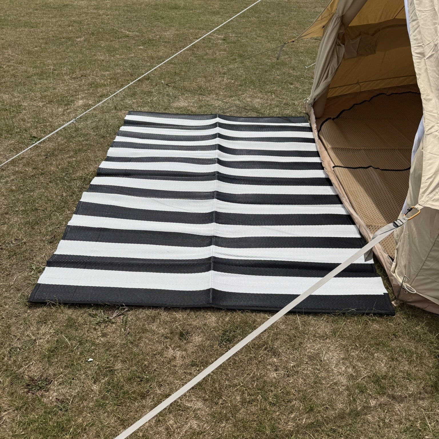Black and white striped mat on grass next to a tent