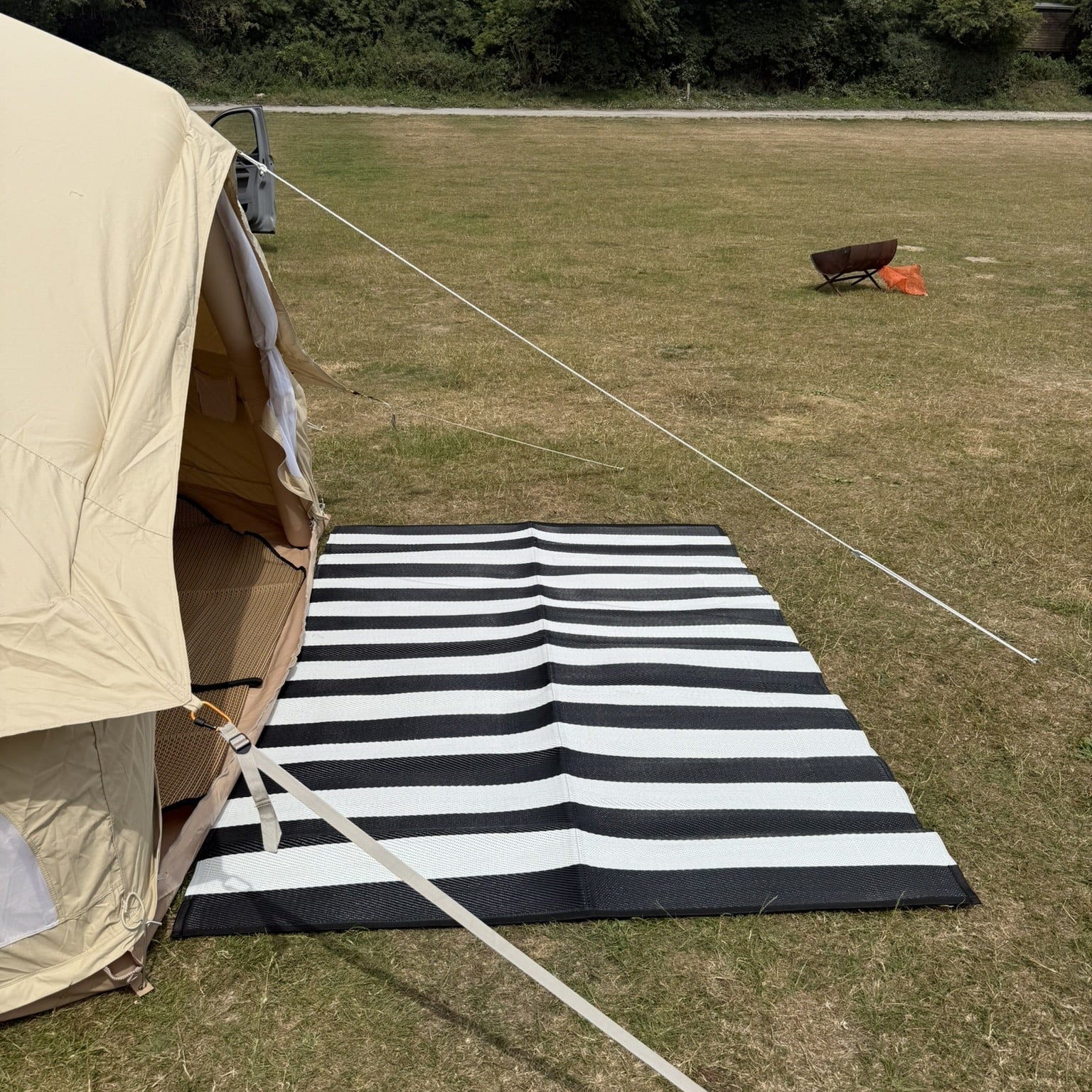 Beige tent with a black and white striped mat on grass