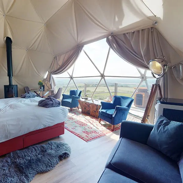 Geodesic dome interior with a bed, sofa, and large windows overlooking a scenic view.