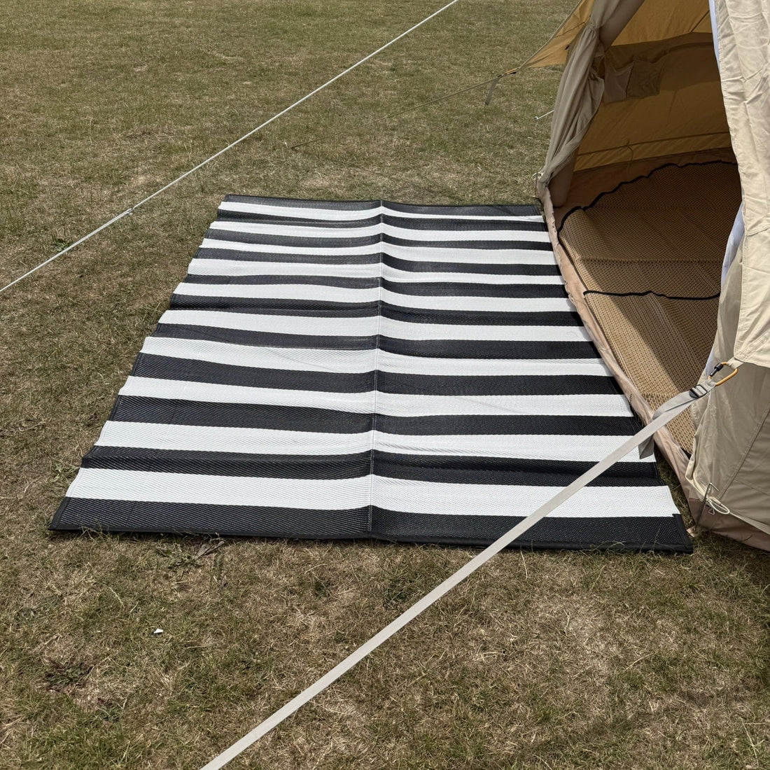 Black and white striped mat on grass next to a tent