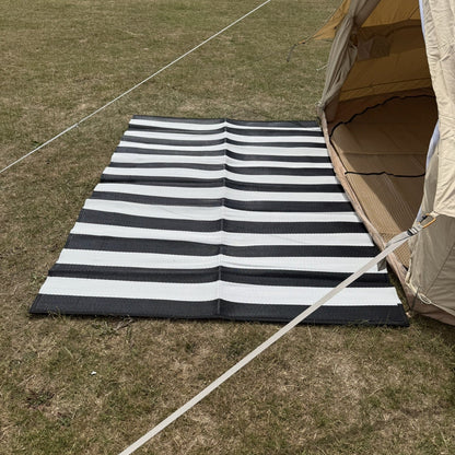 Black and white striped mat on grass next to a tent