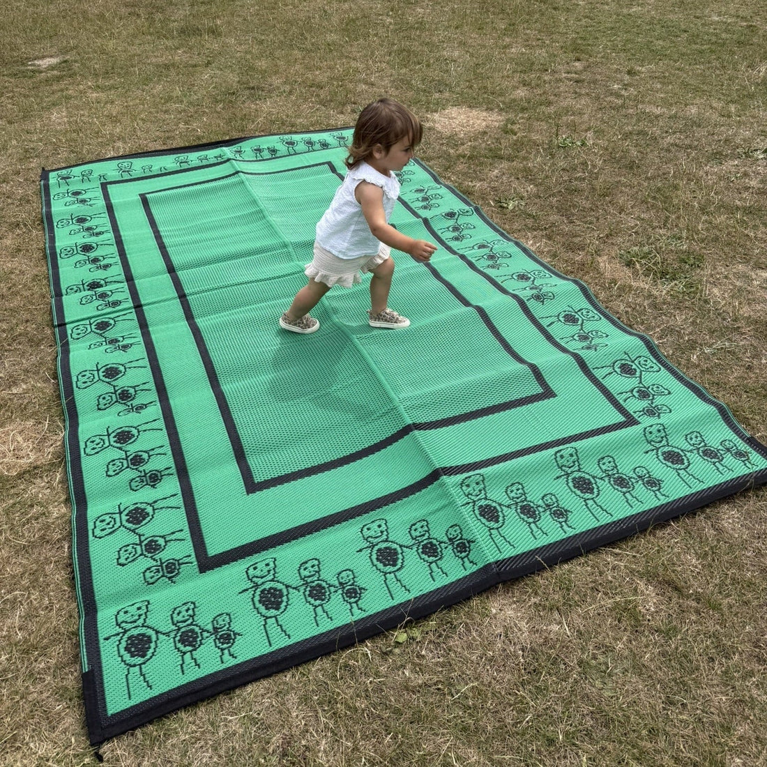 Green kids rectangular camping mat on grass with playful border illustrations, shown in outdoor use