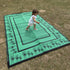 Green kids rectangular camping mat on grass with playful border illustrations, shown in outdoor use